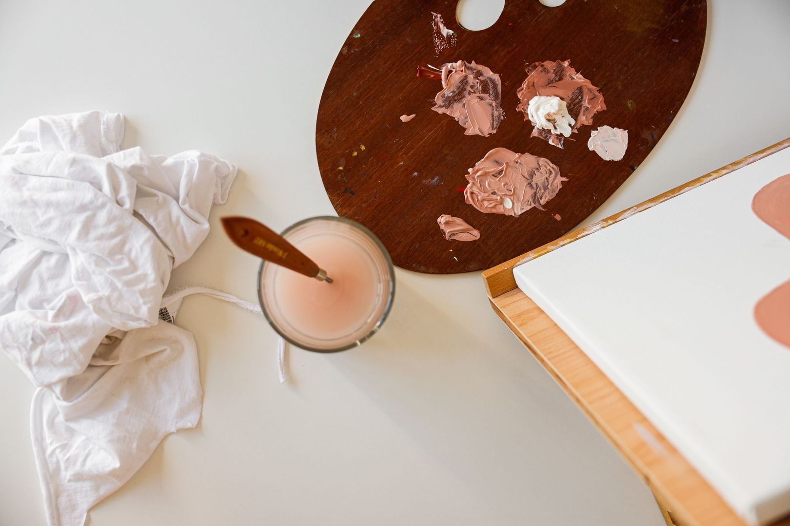 Målarpalett med rosa färger, pensel, duk och vit tygtrasa